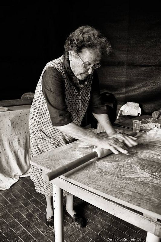 A nonna rolling fresh pasta dough by hand on a floured table